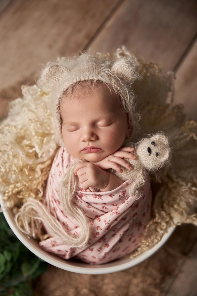Novorozená holčička v bílém kyblíku s květinovým wrapem a sovičkou.