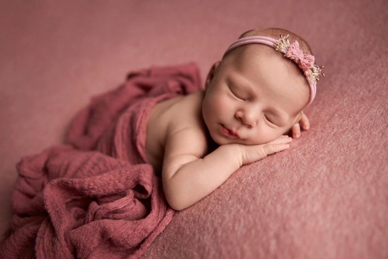 Miminko holčička na bříšku na starorůžovém pozadí s čelenkou.