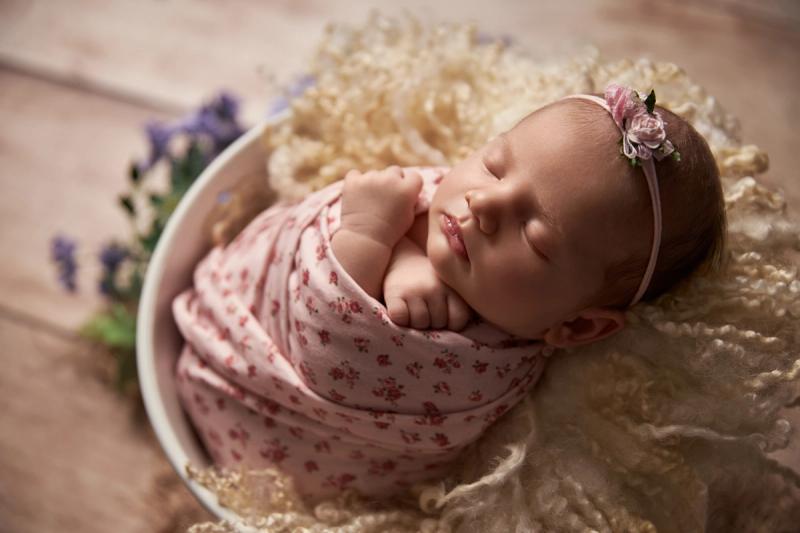 Newborn holčička v bílém kyblíku s růžovým květinovým wrapem a čelenkou.