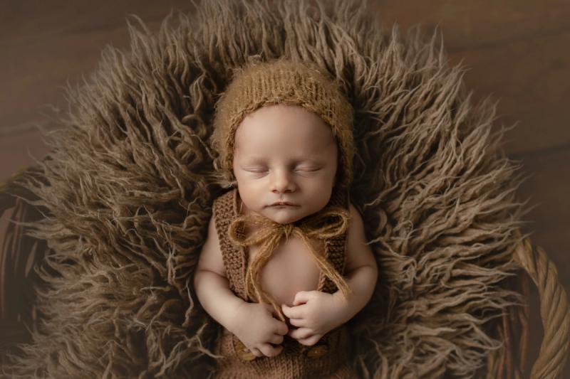 Miminko v košíku v karamelovém pleteném oblečení s čepičkou.