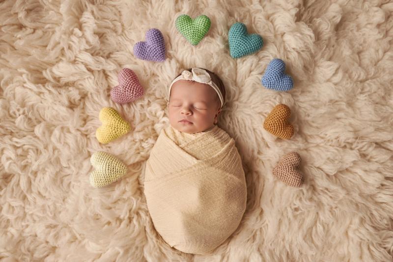Newborn holčička v krémovém wrapu s barevnými srdíčky v fotoateliéru.