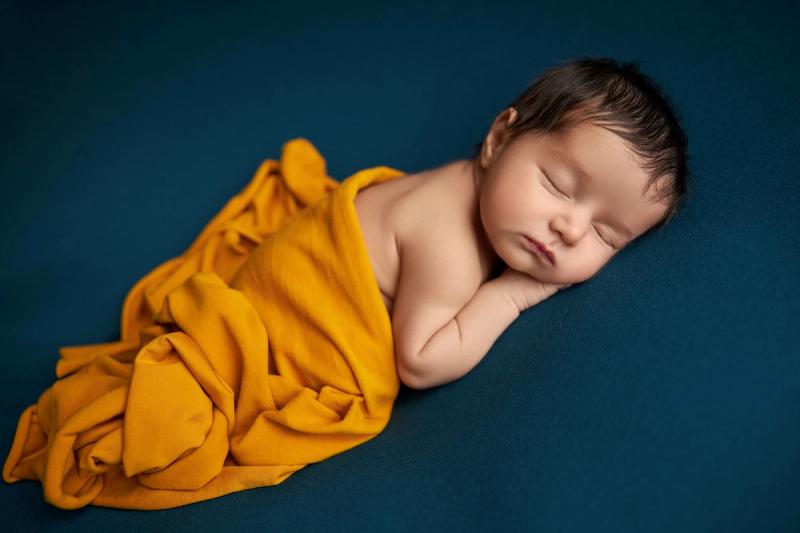 Newborn miminko na modrém pozadí v oranžovém wrapu, záběr z boku.