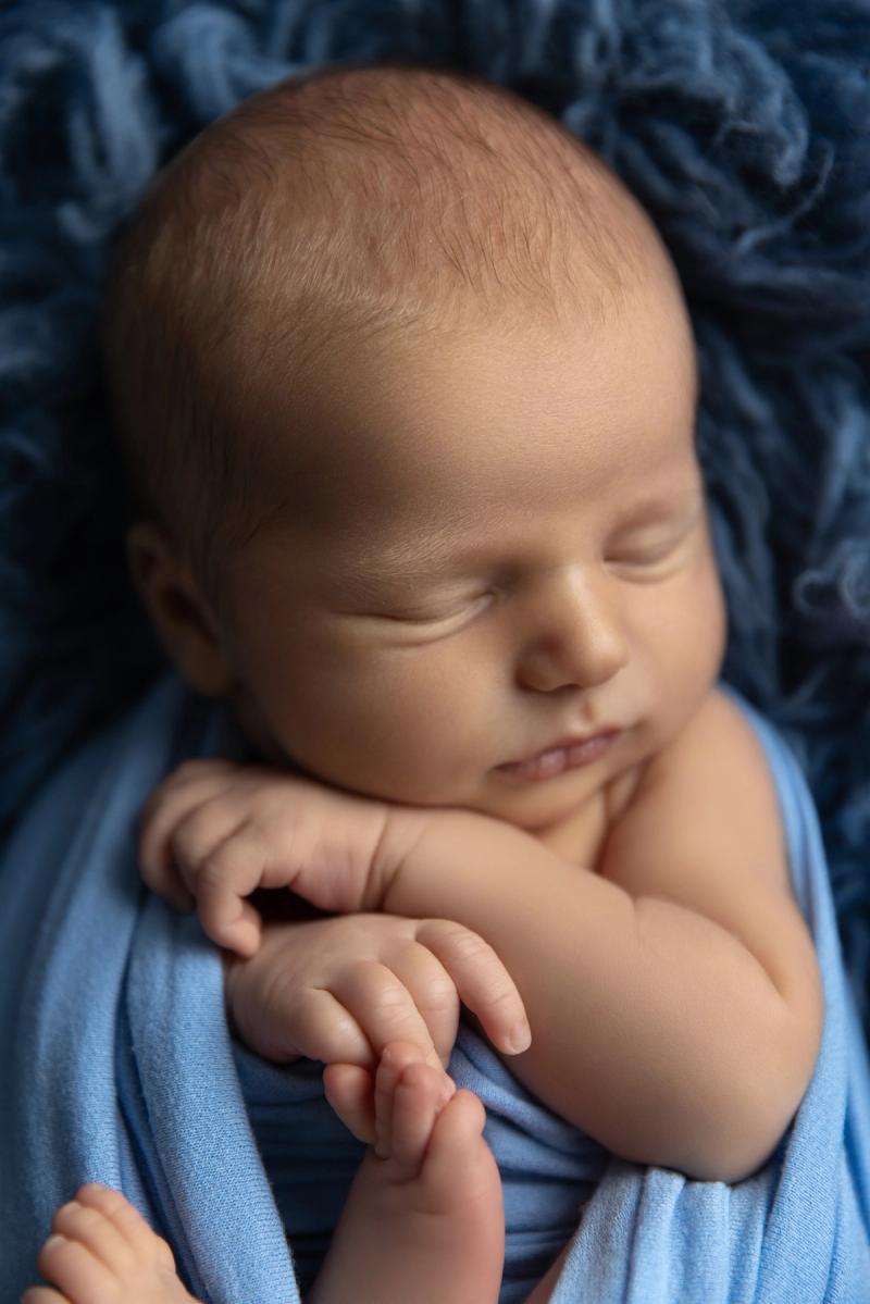Detail obličeje a ručiček novorozence v modrém wrapu.