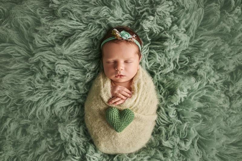 Miminko holčička v zeleném wrapu na zelené kožešině se srdíčkem.