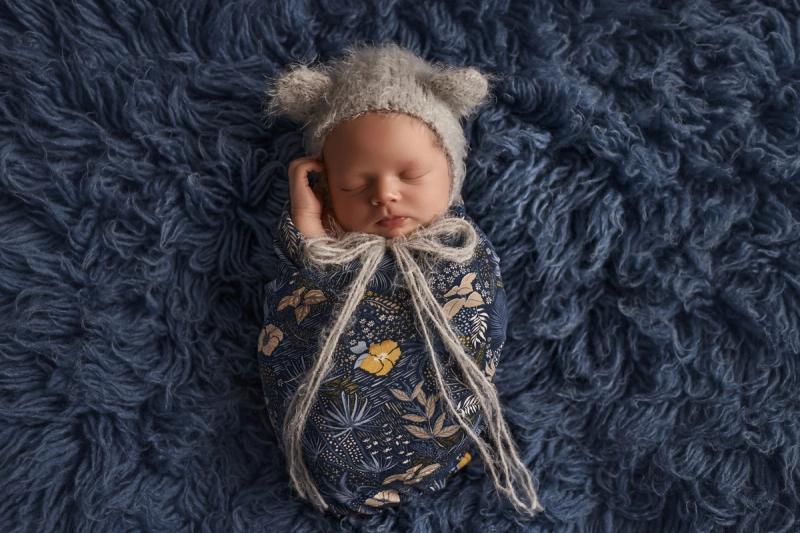 Miminko v tmavě modrém květinovém wrapu s medvědí čepičkou.