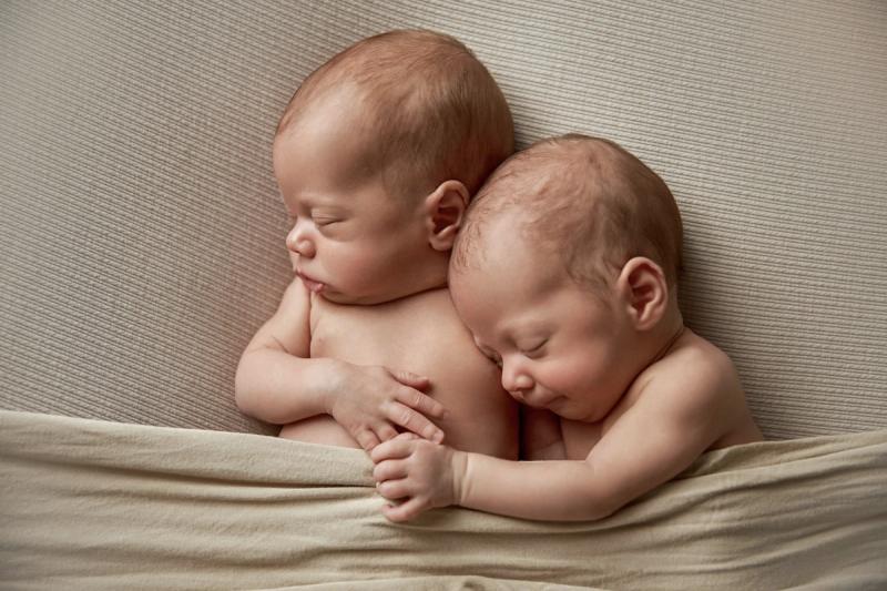 Newborn dvojčata přivinutá k sobě na béžové dece, studio Praha.
