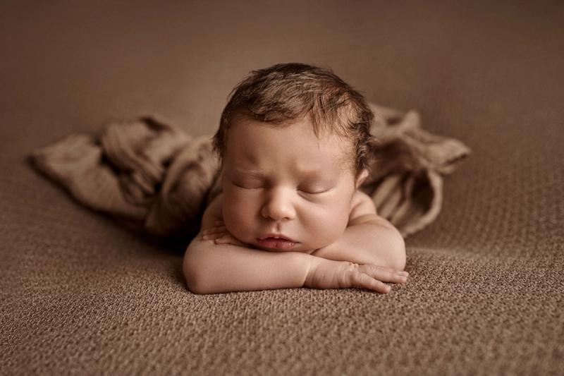 Newborn miminko na bříšku na hnědém pozadí, portrét ze studia.