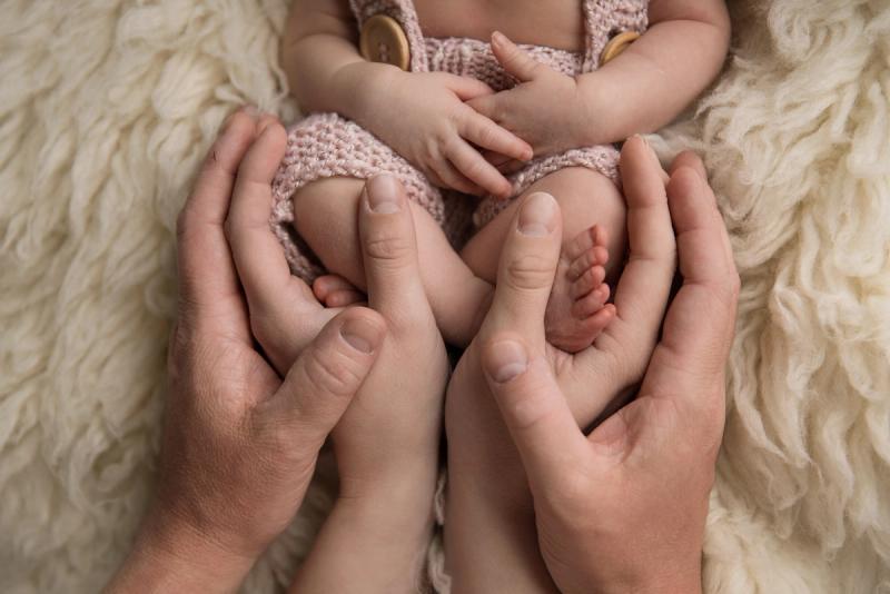 Detail nožiček novorozence v rukou rodičů na béžové kožešině.
