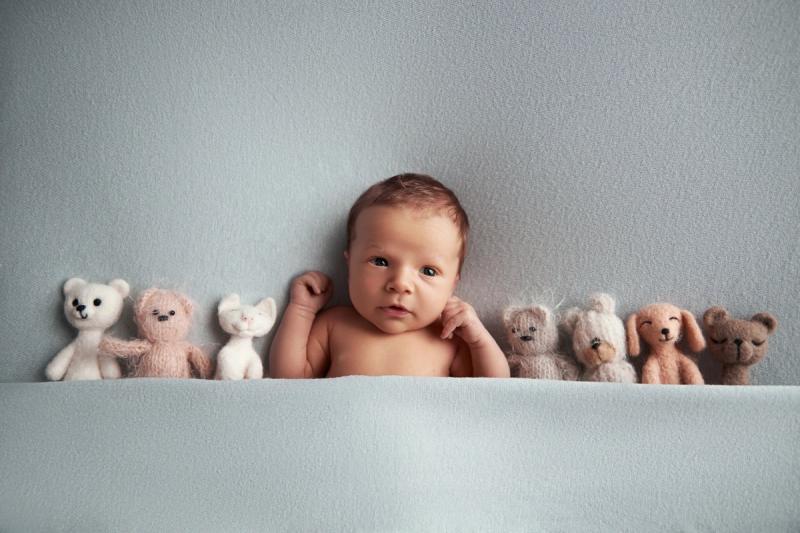 Novorozenec na bříšku s plyšovými hračkami na modrém pozadí.