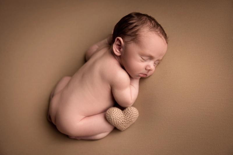 Novorozenec bez oblečení na béžové dece se srdíčkem u nožiček.