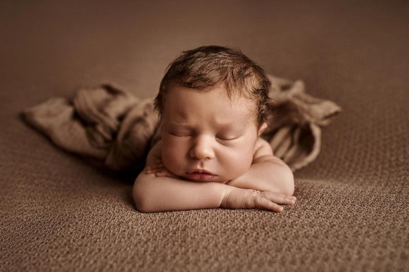 Newborn miminko na bříšku na hnědém pozadí, portrét ze studia.