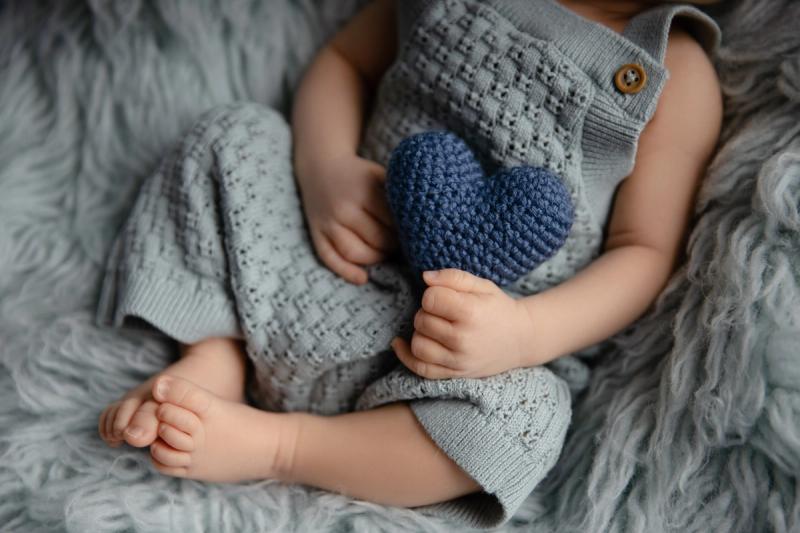 Detail miminka v šedých lacláčích s modrým srdcem v ruce.