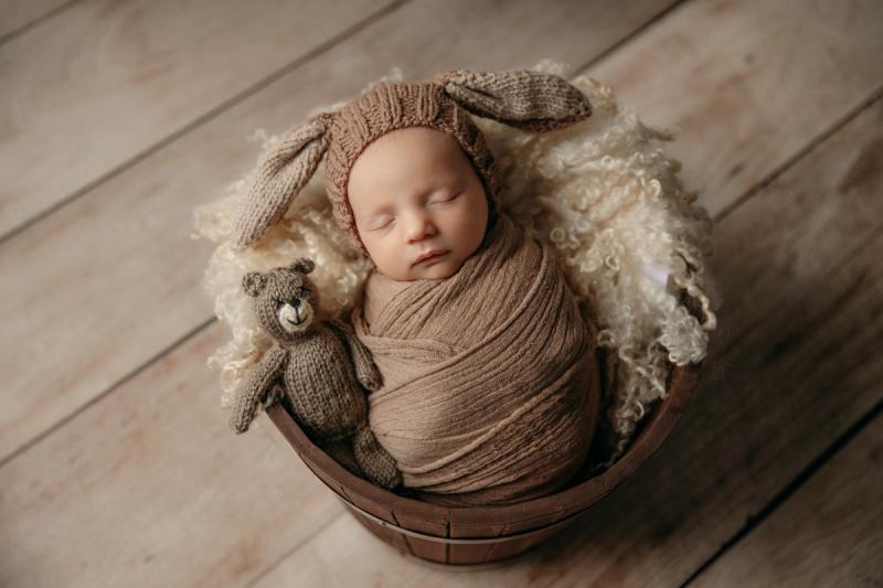Miminko v dřevěném košíku se zaječí čepičkou a medvídkem.