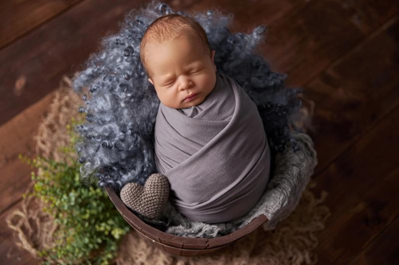 Newborn miminko v dřevěném koši s šedým wrapem a modrou kožešinou.