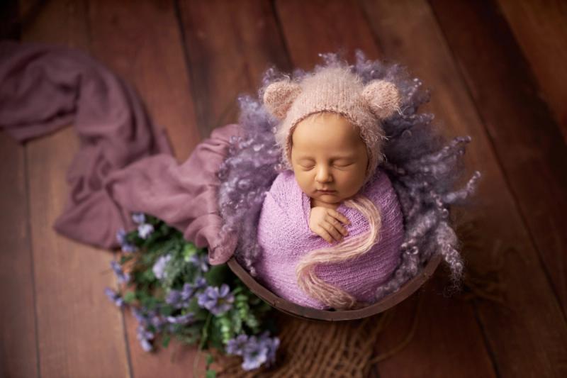 Miminko holčička v košíku s fialovým wrapem a medvědí čepičkou.