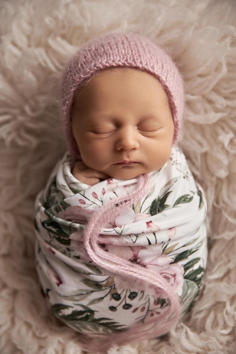 Miminko holčička v květinovém wrapu s růžovou čepičkou na kožešině.