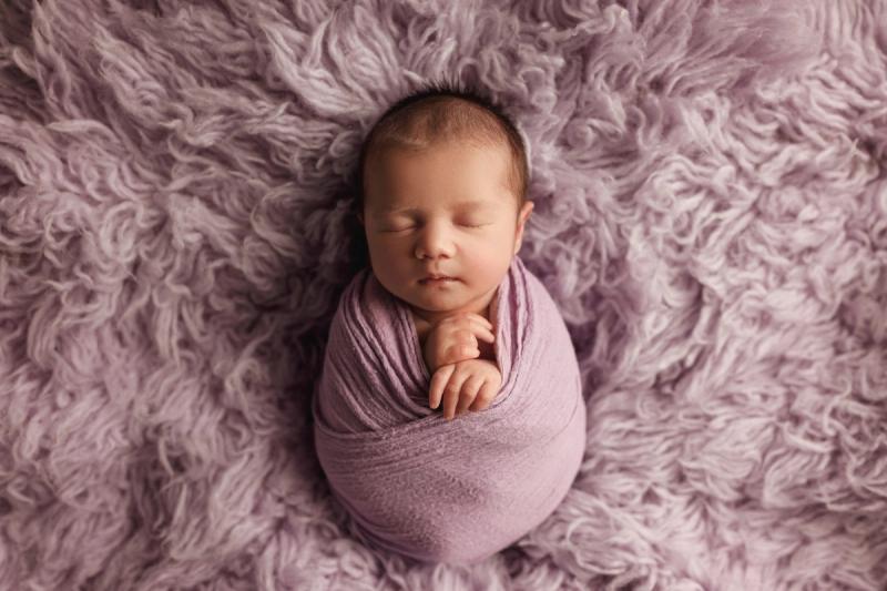 Newborn holčička ve fialovém wrapu na fialové kožešině, fotoateliér Praha.