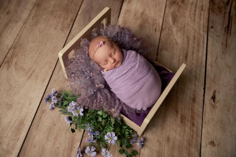Miminko holčička v dřevěné postýlce s fialovým wrapem a levandulí.