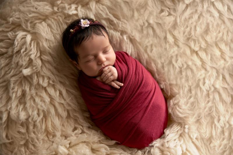 Novorozená holčička v červeném wrapu na béžové kožešině, Praha.