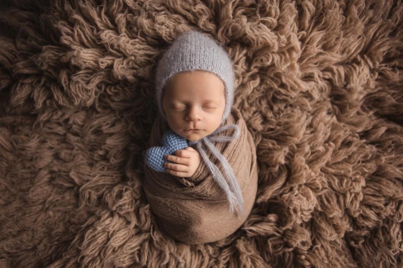 Novorozenec v béžovém wrapu s medvědí čepičkou a modrým srdcem.