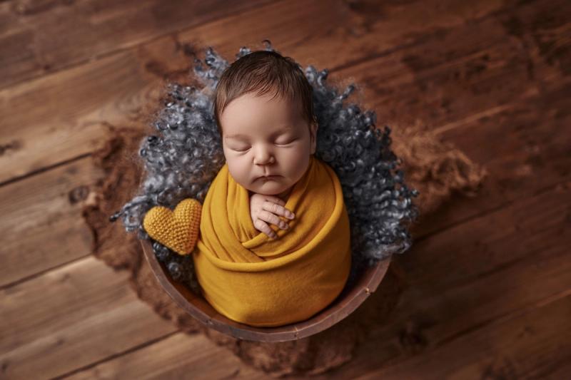 Novorozenec v košíčku v okrovém wrapu na šedé kožešině, Praha.