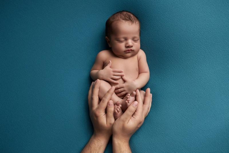 Newborn miminko v rukou rodičů na modrém pozadí, studio Praha.