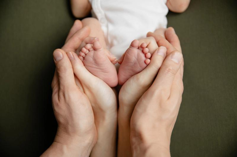 Detail nožiček novorozence v rukou rodičů na zeleném pozadí.