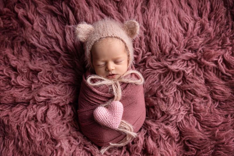 Miminko holčička v růžovém wrapu s medvědí čepičkou a srdíčkem.