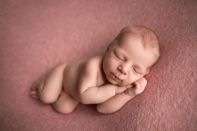 Newborn holčička na bříšku na růžové dece, portrét z fotoateliéru.
