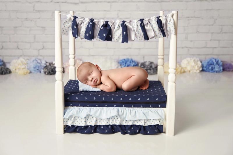 Newborn miminko v postýlce v námořnickém tématu na cihlovém pozadí.