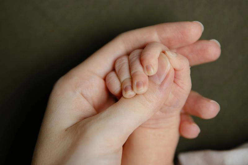 Detail novorozence držícího ruku rodiče na zeleném pozadí.