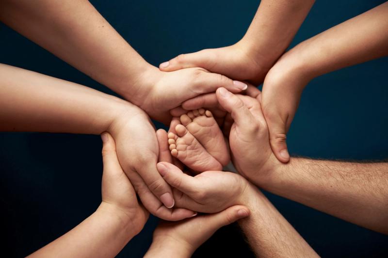 Detail nožiček novorozence v rukou celé rodiny na tmavém pozadí.