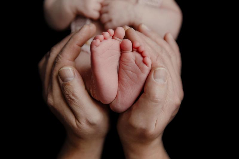 Detail nožiček novorozence v rukou rodiče na černém pozadí.