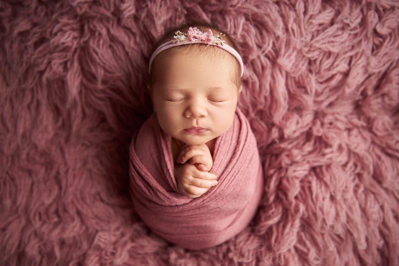 Newborn holčička v růžovém wrapu s květinovou čelenkou.