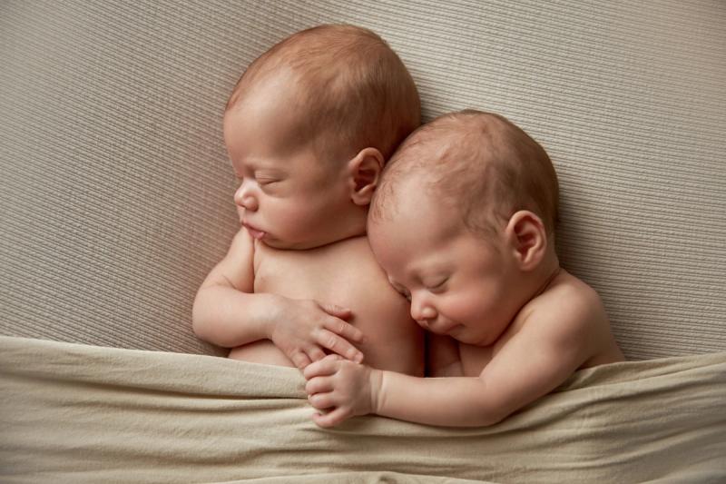 Newborn dvojčata přivinutá k sobě na béžové dece, studio Praha.