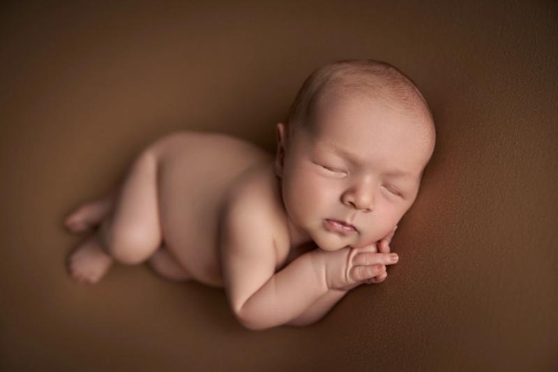 Newborn miminko bez oblečení na hnědém pozadí, portrét z boku.