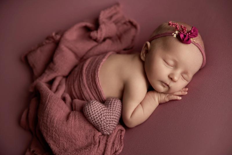 Novorozená holčička na bříšku ve starorůžovém wrapu s čelenkou.