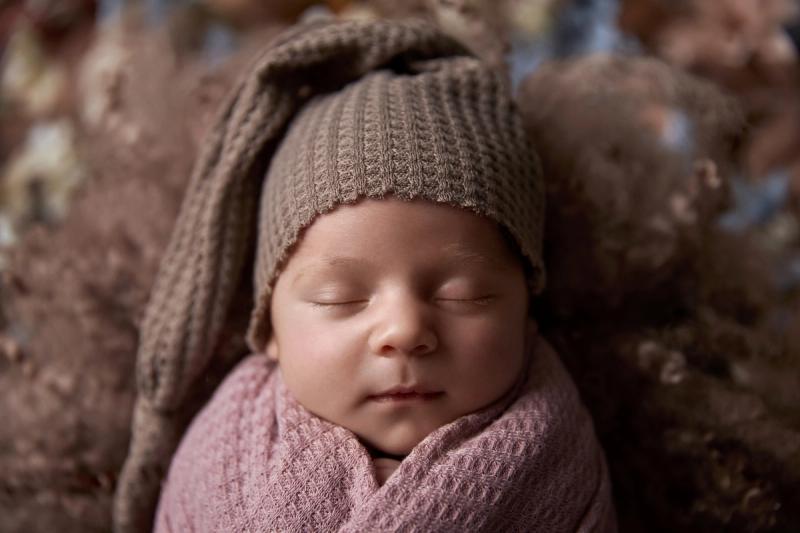 Newborn holčička ve starorůžovém wrapu se šátkem s ušima a květinami.