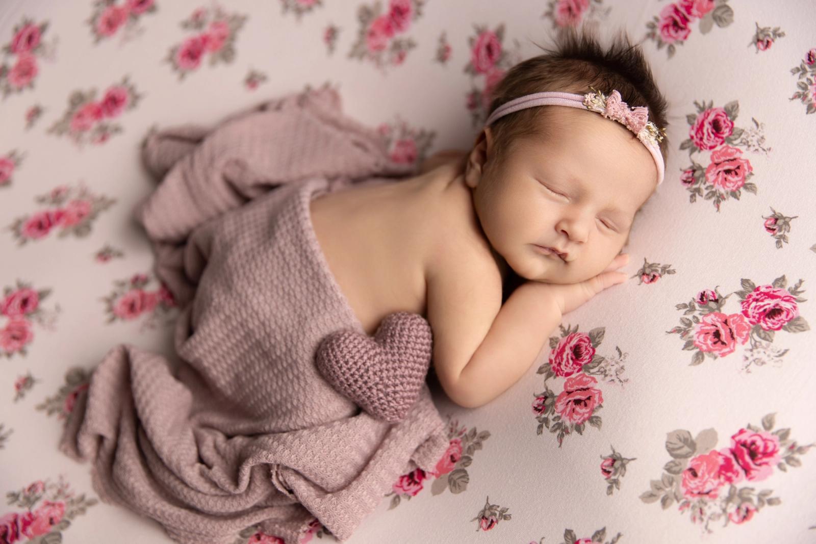 newbon ležící miminko s čelenkou na červeném podkladu