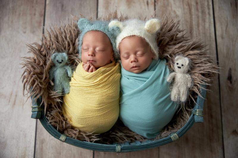 Novorozená dvojčata v košíku ve žlutém a tyrkysovém wrapu.