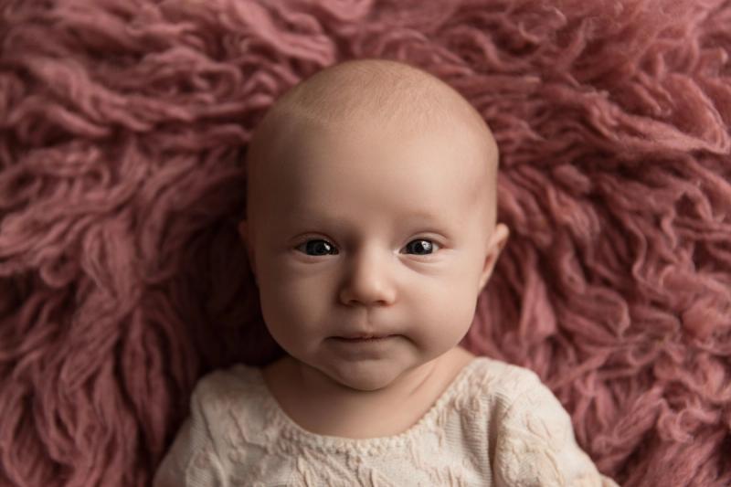 Tříměsíční miminko na růžové kožešině, pohled do kamery.