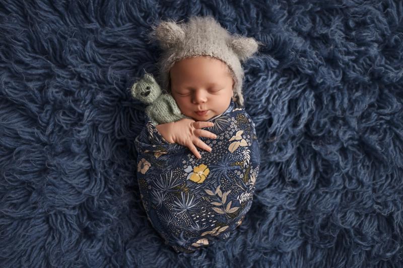 Newborn miminko v tmavě modrém květinovém wrapu se zelenou čepičkou.