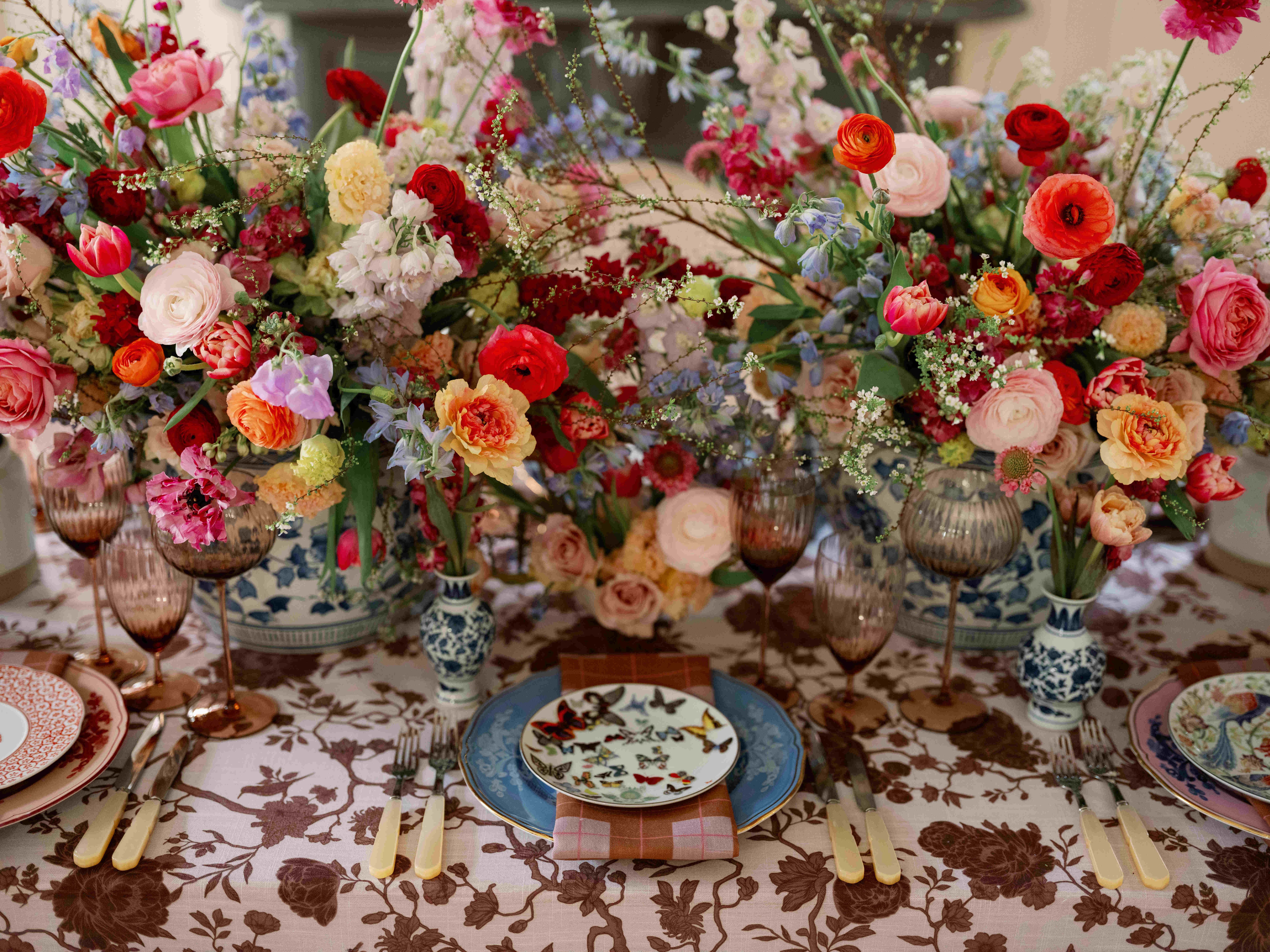 Floral patterned table linen beneath colorful flowers and layered place settings.