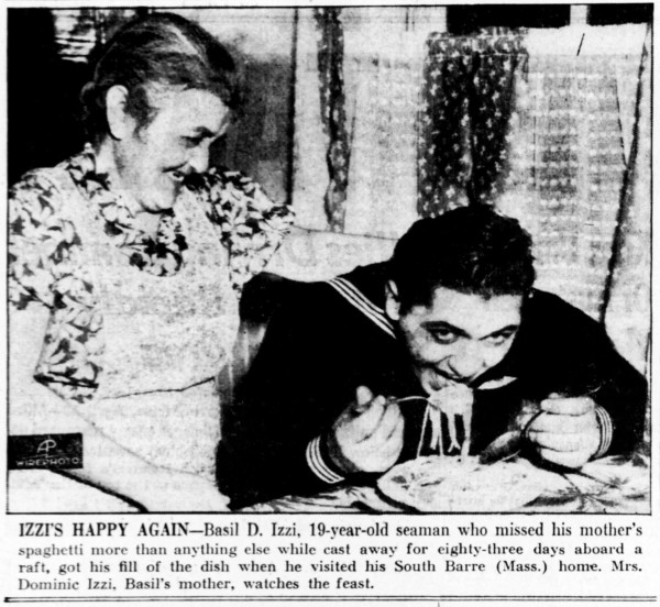 Basil Izzi sittin at a table with a fork-full of spaghetti in his mouth. His mother stands behind him with her hand on his shoulder.