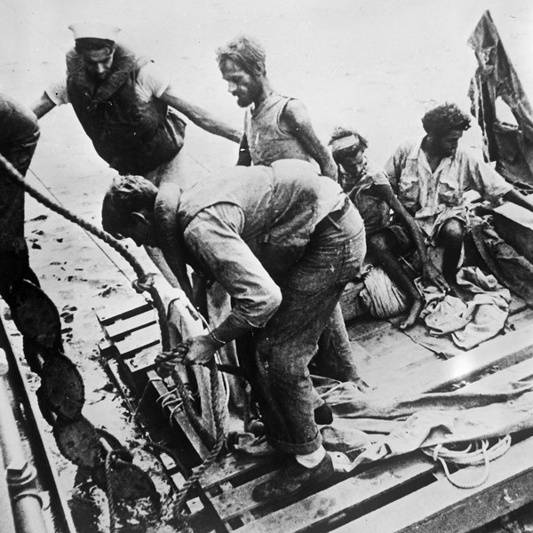 Two sailors helping a very skinny man with a bread off a raft onto a boat. Two other skinny men sit on the raft waiting to be helped.