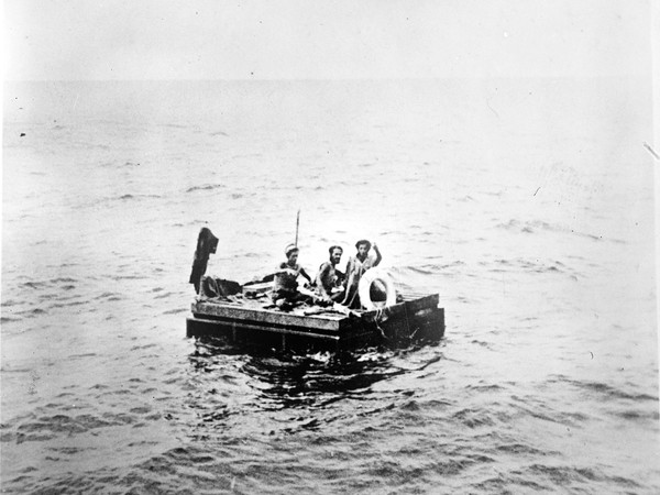 Three men on a wooden raft in the ocean.