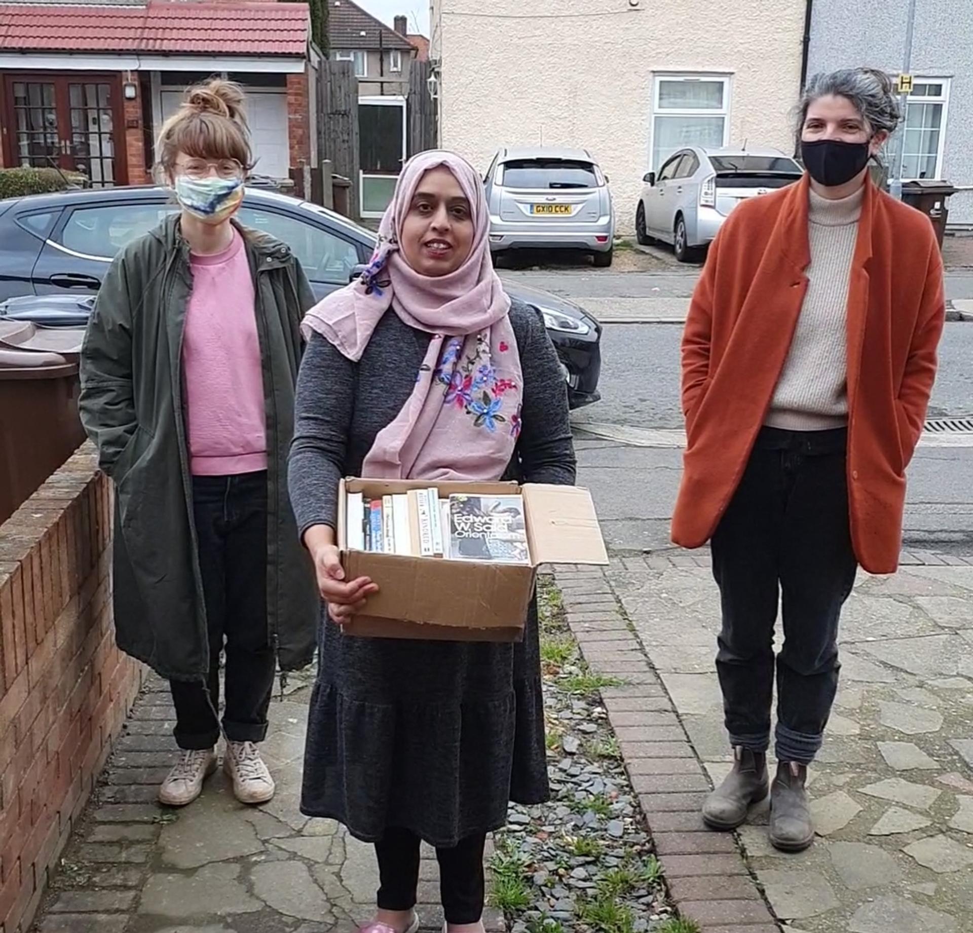 Farzana holding a box of books with Ruth and Amy standing either side