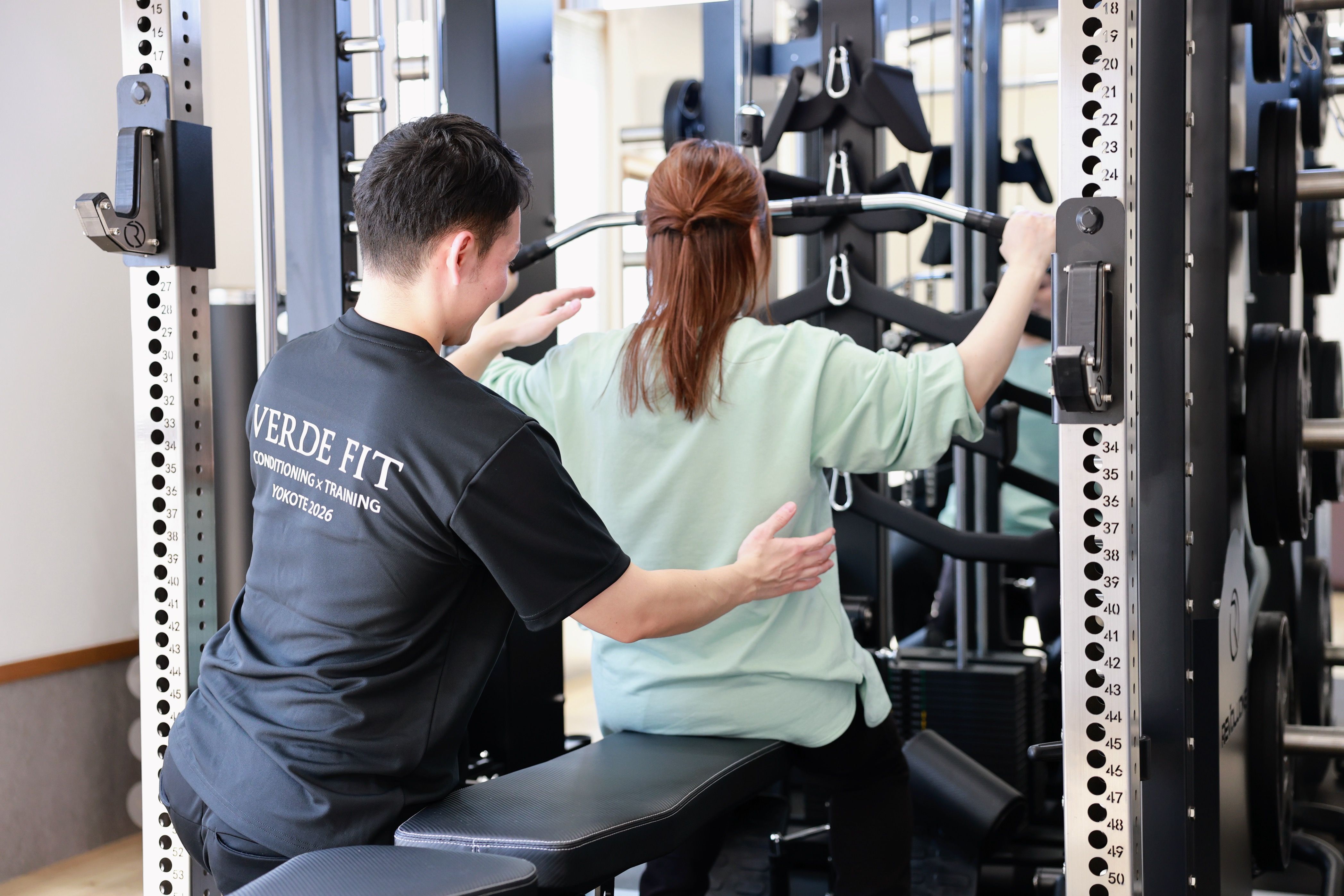 横手市パーソナルジムVERDEFITでトレーナーがマシントレーニングをサポートする様子