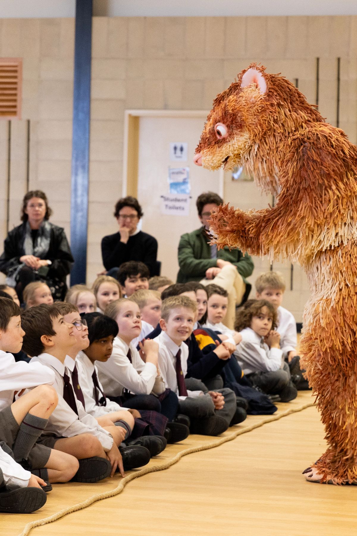 Feathers a giant ferret, is in front of a group of students from Scotch Oakburn College, these young students look up in awe at the giant ferret puppet!