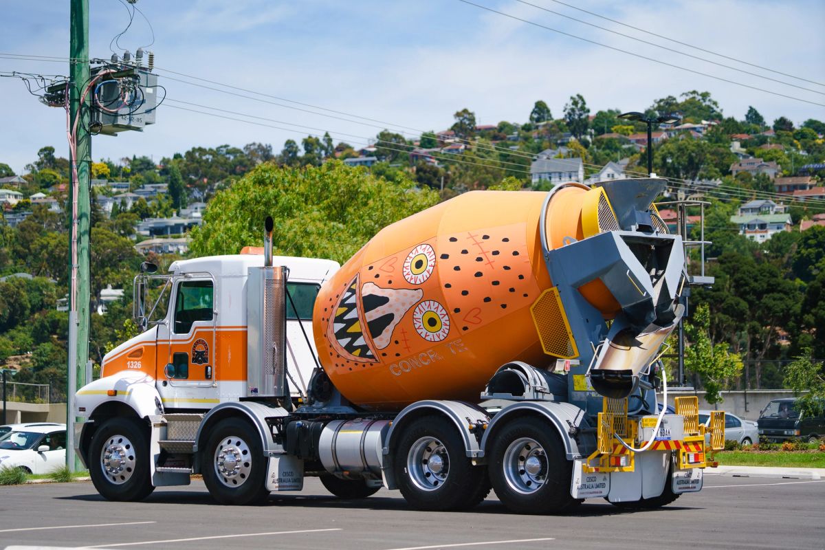 An orange cement mixer with graphic design of a face on the side of it sits parked in a car park